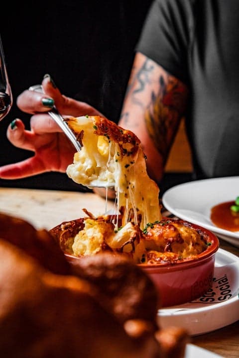 Bubbling cauliflower cheese being lifted from a Ten Streets Social dish
