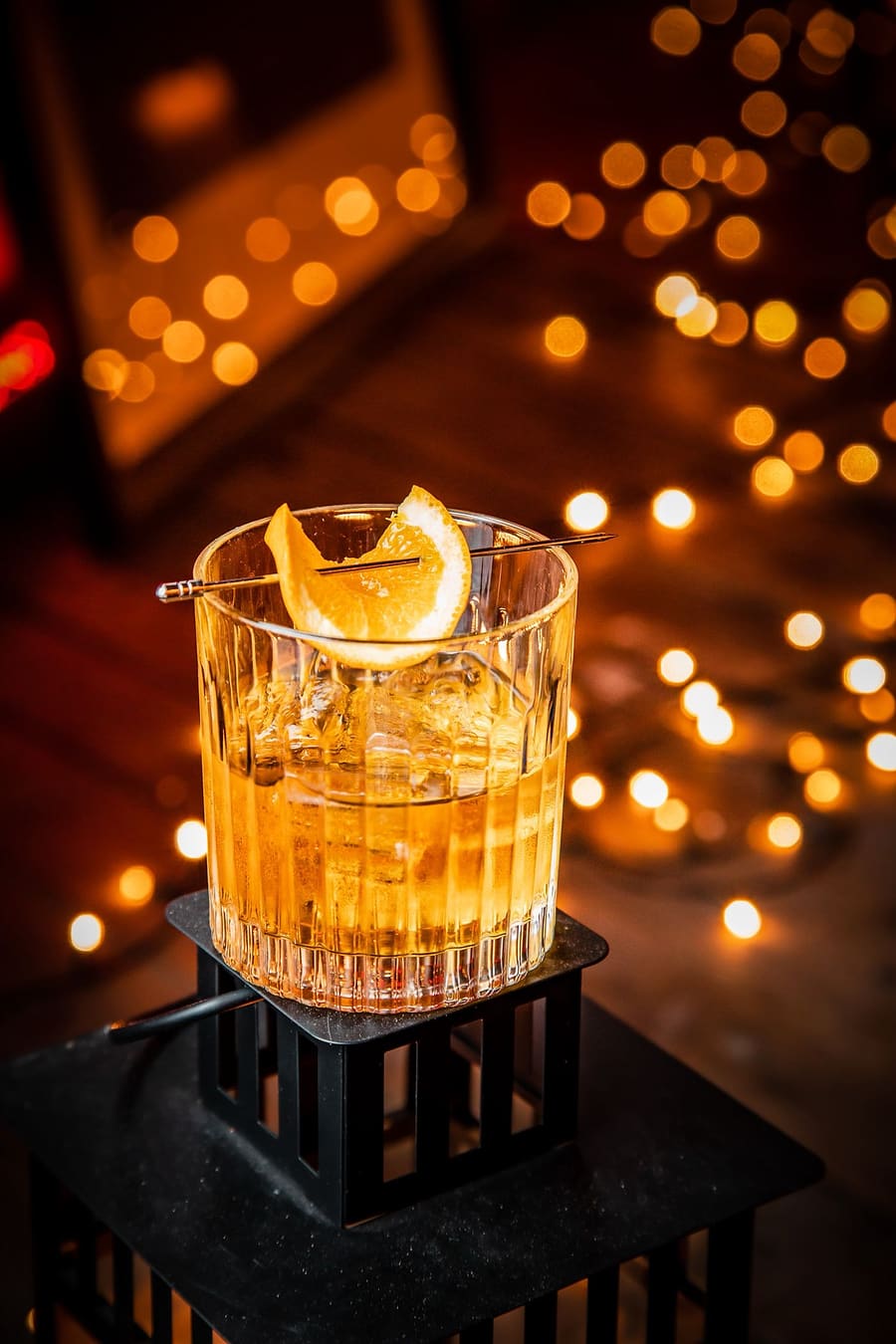 An amber cocktail over ice with an orange twist at the Ten Streets Social bar, fairy lights behind