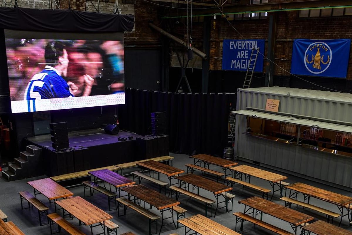 The main hall at Ten Streets Social set with rows of long tables and benches in front of the big screen and stage