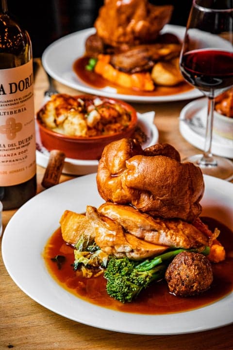 A roast plate with a towering Yorkshire pudding, roast potatoes, broccoli and gravy beside a glass of red wine